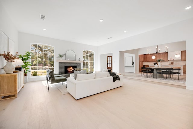 living area with light wood-style flooring, recessed lighting, a notable chandelier, visible vents, and a brick fireplace