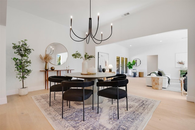 dining room featuring a chandelier, visible vents, a towering ceiling, and wood finished floors