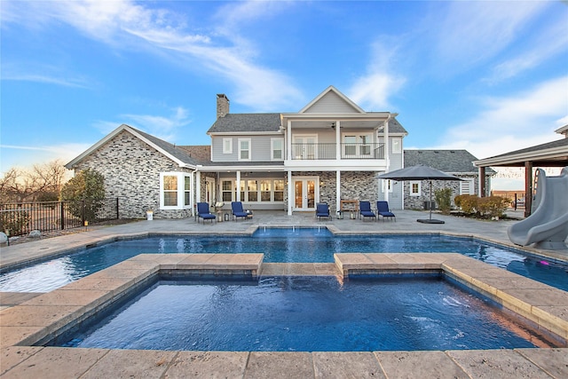 back of house featuring a chimney, stone siding, an in ground hot tub, and french doors