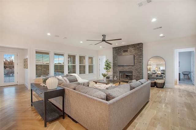 living room featuring ceiling fan, baseboards, a stone fireplace, and visible vents