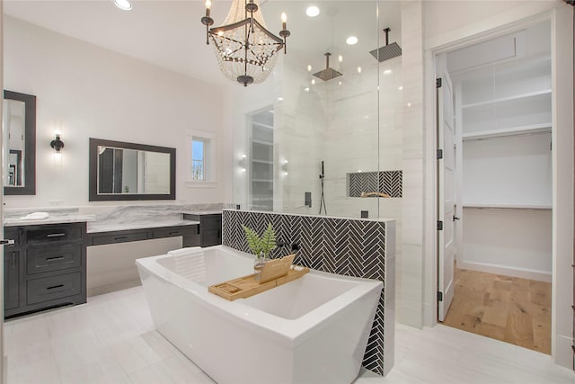 bathroom featuring an inviting chandelier, a tile shower, vanity, a freestanding tub, and a spacious closet