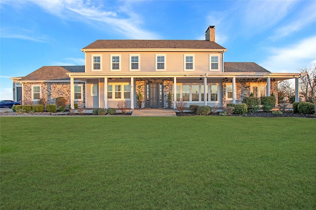rear view of property with a yard, a chimney, ceiling fan, stone siding, and a porch