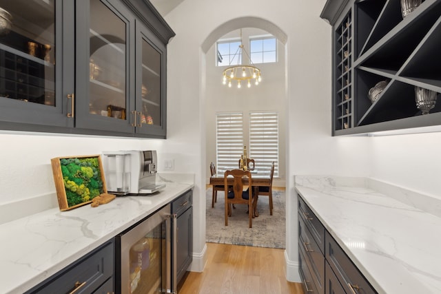 bar with a notable chandelier, beverage cooler, and light wood-type flooring