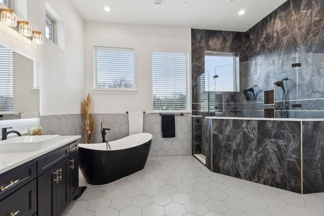 full bathroom featuring vanity, a freestanding tub, a walk in shower, tile walls, and tile patterned floors