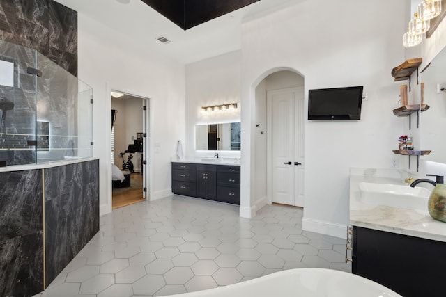 ensuite bathroom featuring tile patterned flooring, walk in shower, two vanities, a soaking tub, and a sink