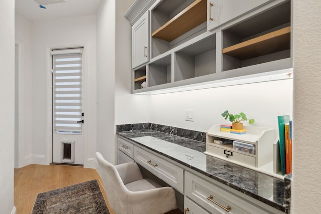 kitchen featuring open shelves, dark stone countertops, built in desk, and light wood finished floors