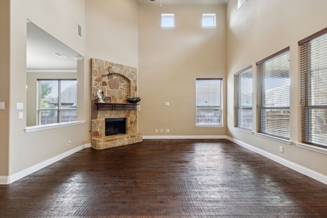 unfurnished living room with a wealth of natural light, baseboards, wood finished floors, and a stone fireplace