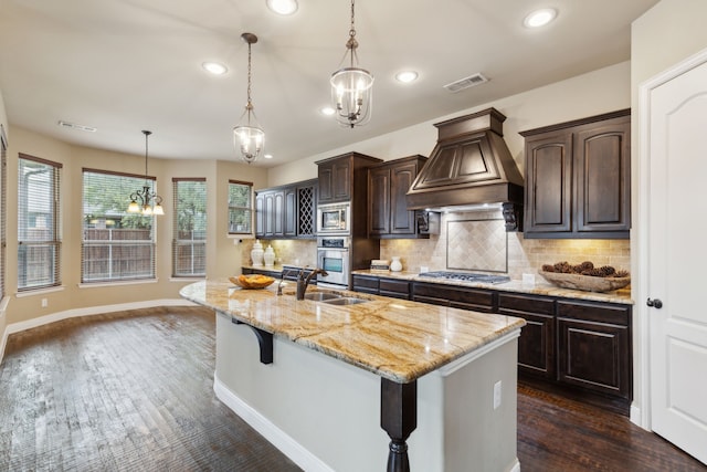 kitchen featuring stainless steel appliances, visible vents, a sink, dark brown cabinetry, and premium range hood