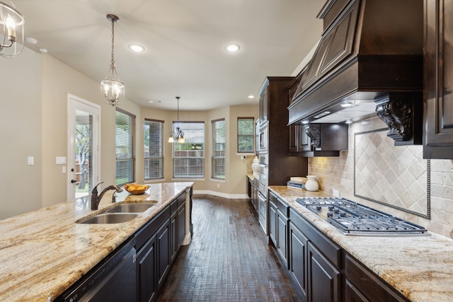 kitchen featuring dark brown cabinetry, light stone countertops, stainless steel appliances, premium range hood, and a sink