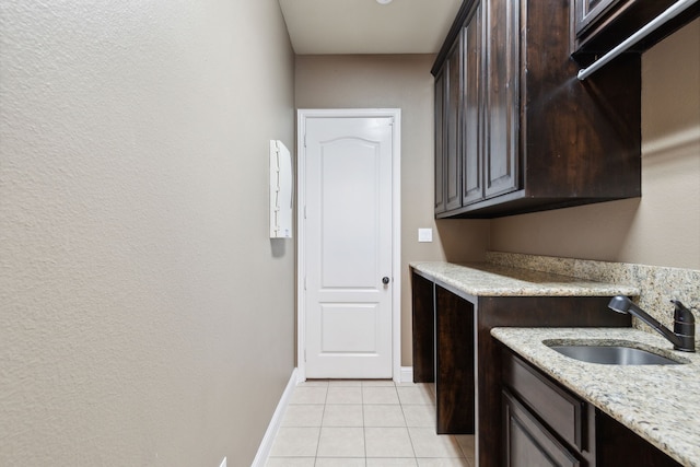 kitchen with light stone counters, light tile patterned flooring, a sink, dark brown cabinets, and baseboards