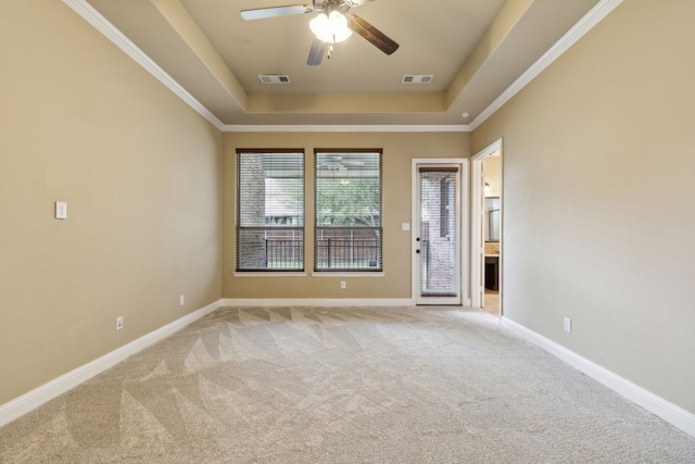 carpeted empty room with ceiling fan, a tray ceiling, visible vents, and baseboards