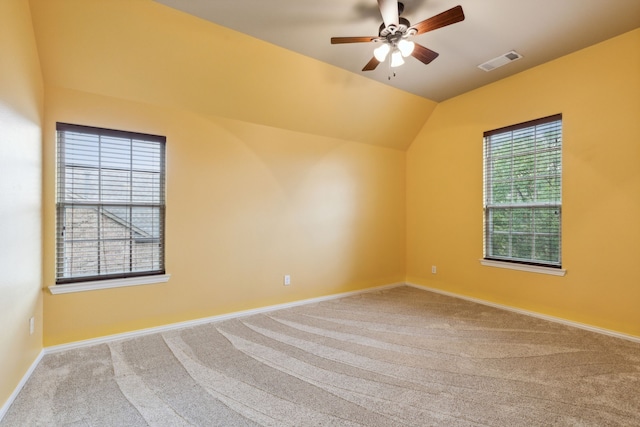 carpeted spare room featuring baseboards, visible vents, vaulted ceiling, and a ceiling fan