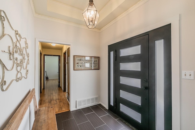 entrance foyer featuring ornamental molding, dark wood-style flooring, a raised ceiling, and visible vents