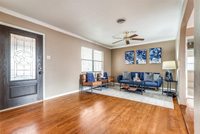 living area with baseboards, ceiling fan, wood finished floors, and crown molding