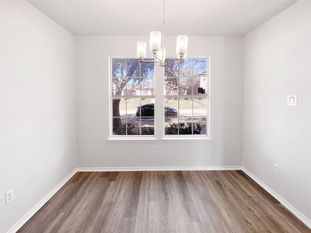 unfurnished dining area featuring baseboards, a chandelier, and wood finished floors