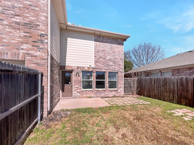 back of house featuring a fenced backyard, a lawn, a patio, and brick siding