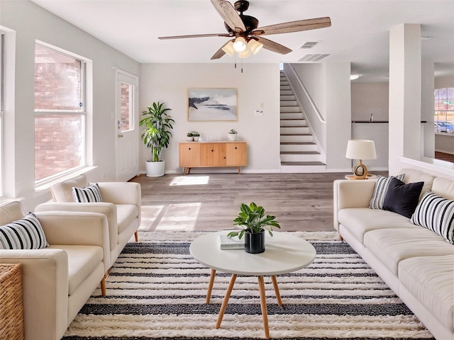 living room featuring wood finished floors, visible vents, a ceiling fan, stairs, and baseboards