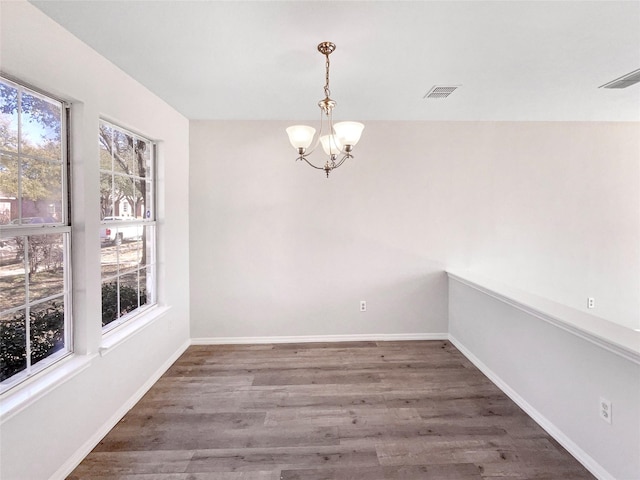 empty room with baseboards, visible vents, a chandelier, and wood finished floors