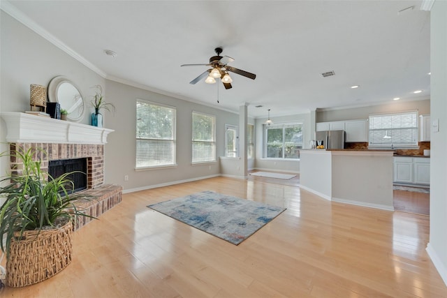 living room with crown molding, visible vents, light wood-style flooring, a brick fireplace, and ceiling fan