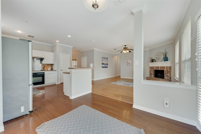 kitchen with freestanding refrigerator, a brick fireplace, white cabinets, wood finished floors, and oven