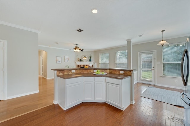 kitchen featuring arched walkways, decorative light fixtures, crown molding, white cabinets, and wood finished floors