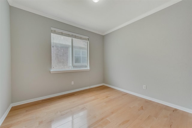 empty room with crown molding, light wood finished floors, and baseboards