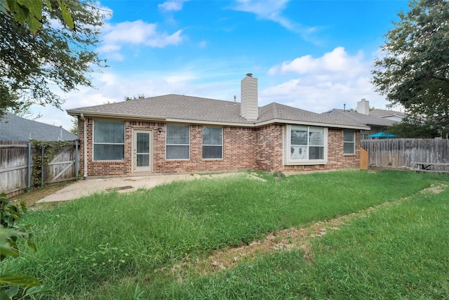 back of house featuring a chimney, brick siding, a yard, and a fenced backyard