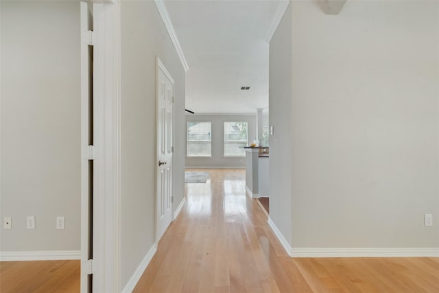 corridor featuring ornamental molding, baseboards, visible vents, and light wood finished floors