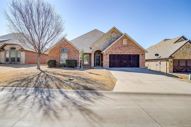 view of front facade with concrete driveway, stone siding, roof with shingles, an attached garage, and brick siding