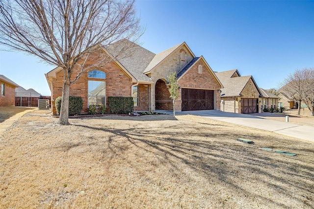 view of front of home with central AC unit, a garage, brick siding, driveway, and stone siding