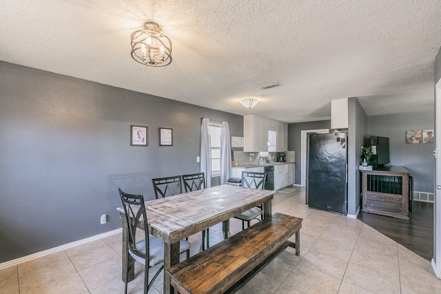 dining area featuring a textured ceiling, light tile patterned flooring, visible vents, baseboards, and an inviting chandelier