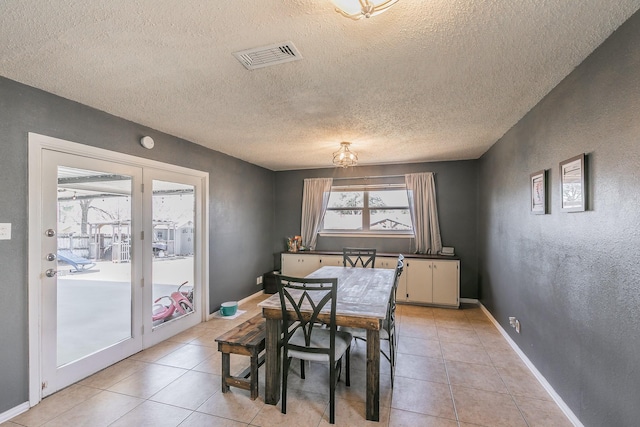 dining room featuring visible vents, a textured wall, baseboards, and light tile patterned floors