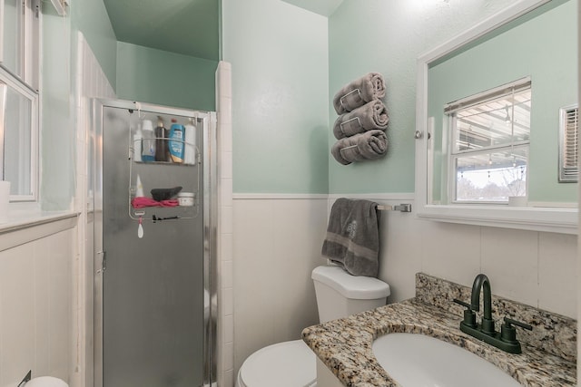 bathroom with a stall shower, a wainscoted wall, vanity, and toilet