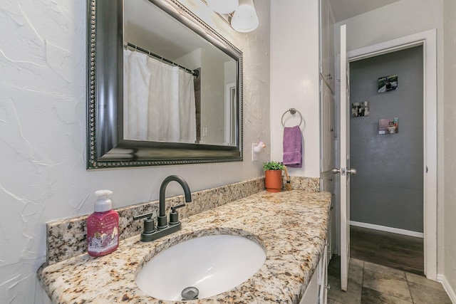 full bathroom with stone finish flooring, baseboards, and vanity