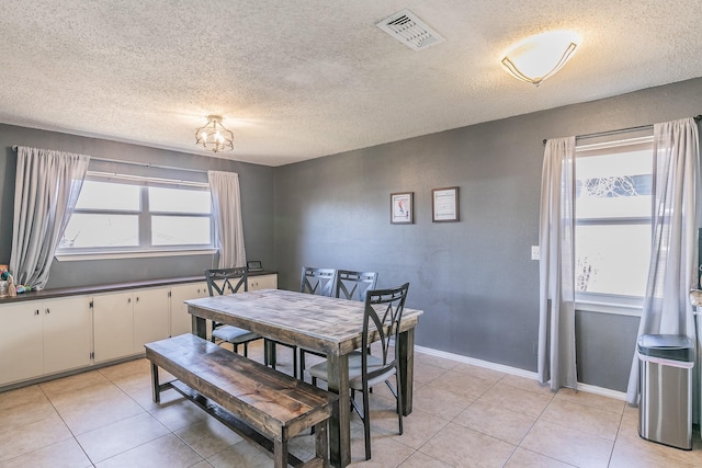 dining area with a textured ceiling, light tile patterned flooring, visible vents, and baseboards