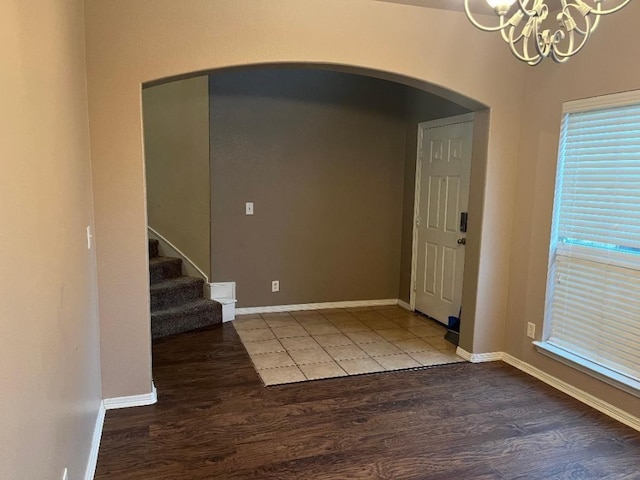 entryway with arched walkways, a notable chandelier, stairway, wood finished floors, and baseboards