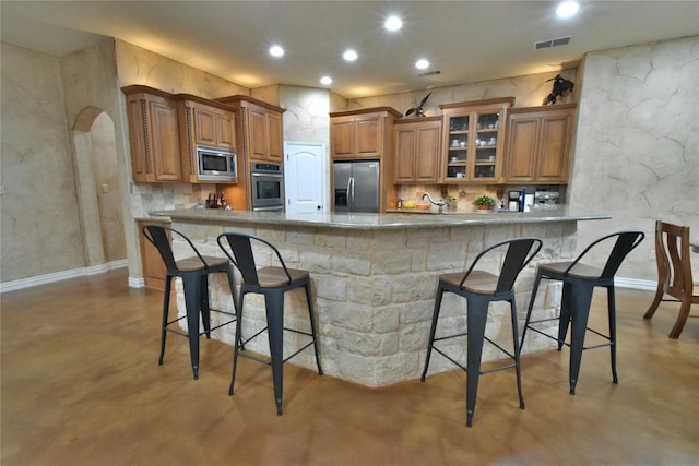 kitchen with finished concrete floors, appliances with stainless steel finishes, brown cabinetry, and arched walkways