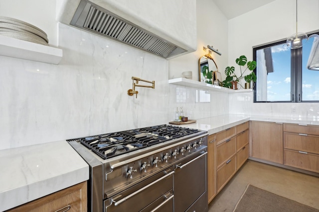 kitchen with high end stainless steel range, hanging light fixtures, ventilation hood, concrete flooring, and backsplash