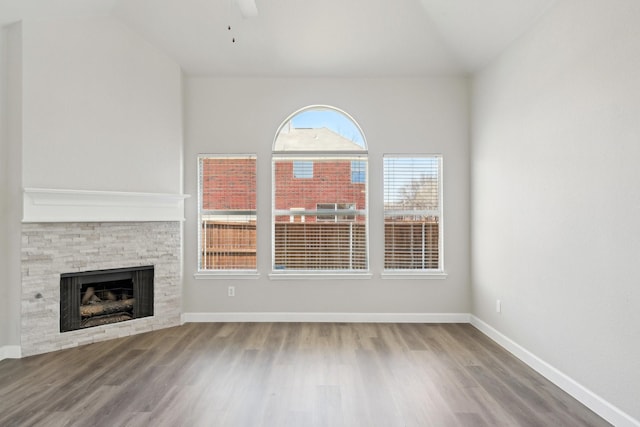 unfurnished living room with a fireplace, a ceiling fan, vaulted ceiling, wood finished floors, and baseboards