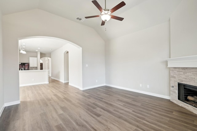 unfurnished living room with visible vents, arched walkways, lofted ceiling, wood finished floors, and a fireplace