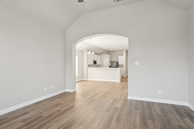 unfurnished living room with arched walkways, ceiling fan, light wood-type flooring, and lofted ceiling