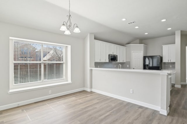 kitchen with light wood-style flooring, stainless steel microwave, black refrigerator with ice dispenser, light countertops, and backsplash