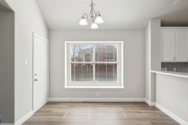 unfurnished dining area featuring light wood-type flooring, an inviting chandelier, and baseboards