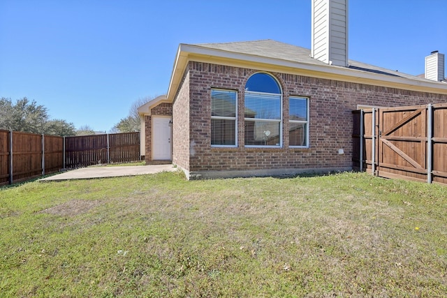 back of house featuring a yard, a fenced backyard, a patio, and brick siding