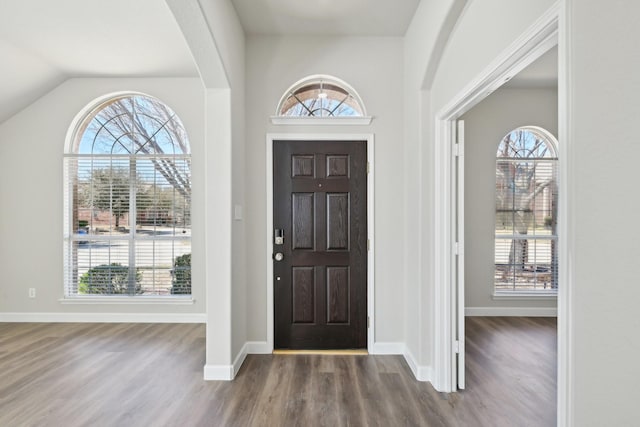 foyer entrance with lofted ceiling, arched walkways, wood finished floors, and baseboards