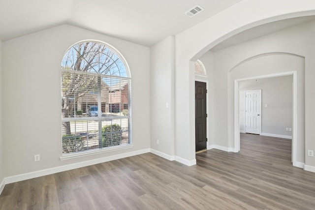 spare room featuring visible vents, plenty of natural light, baseboards, and wood finished floors