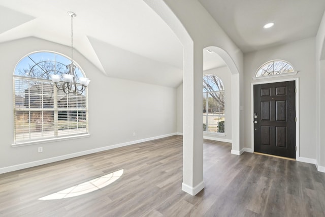 foyer entrance with arched walkways, vaulted ceiling, wood finished floors, a chandelier, and baseboards