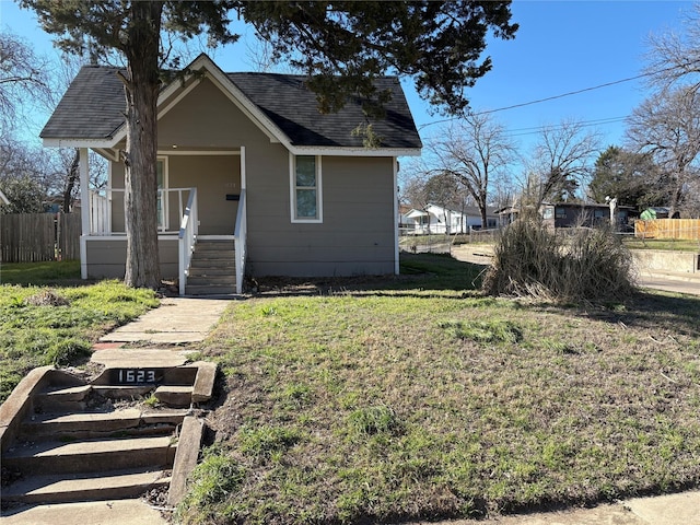 view of front facade with a front lawn, roof with shingles, and fence