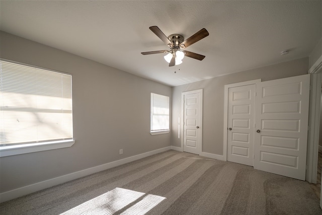 unfurnished bedroom with light carpet, two closets, a ceiling fan, and baseboards