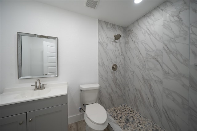 bathroom featuring visible vents, toilet, vanity, tiled shower, and baseboards